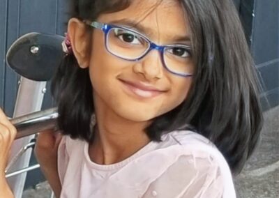 Riya is wearing blue eye glasses and smiling at the camera